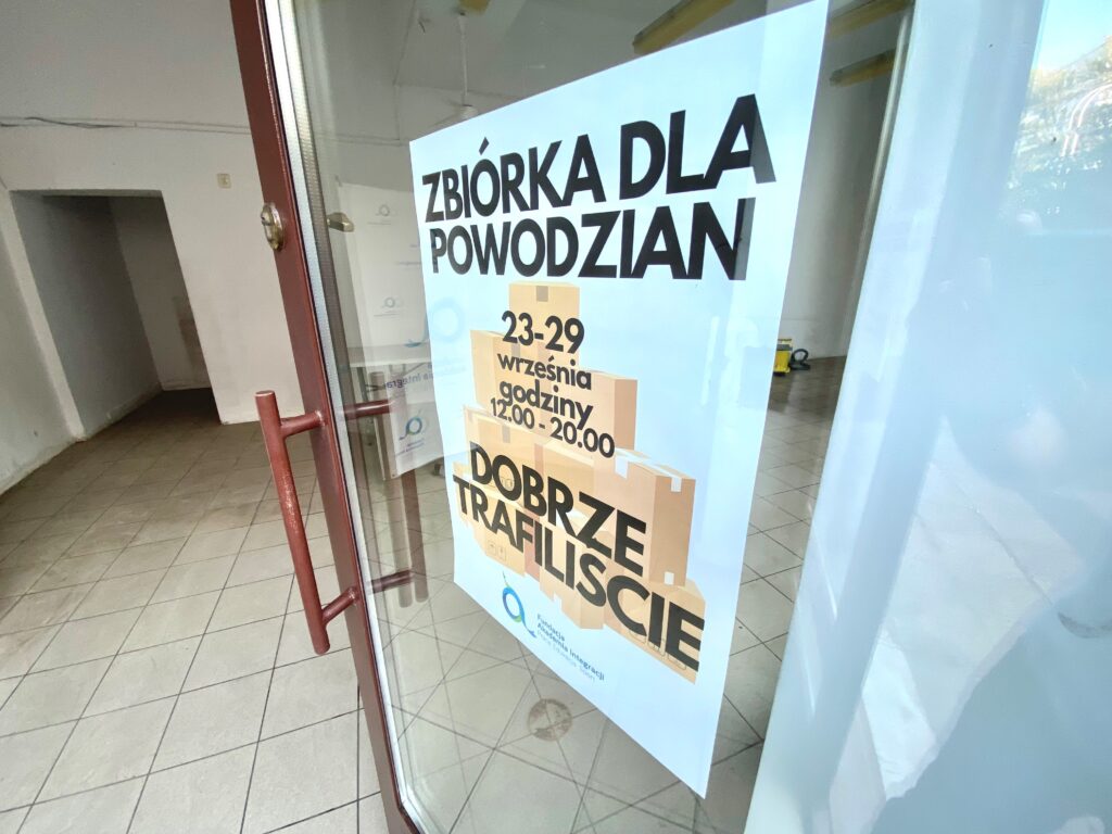 zdjęcie przedstawiające otwarte drzwi z plakatem z napisem "zbiórka dla powodzian"